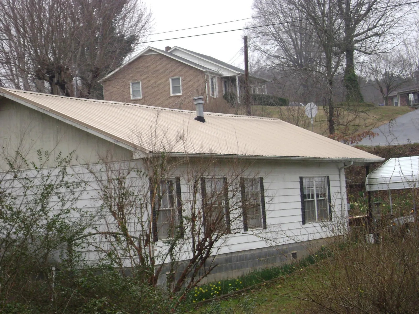 Tan metal roof on a white sided house set into a hillside — Commercial Roofing by Roofing Brothers in Las Vegas